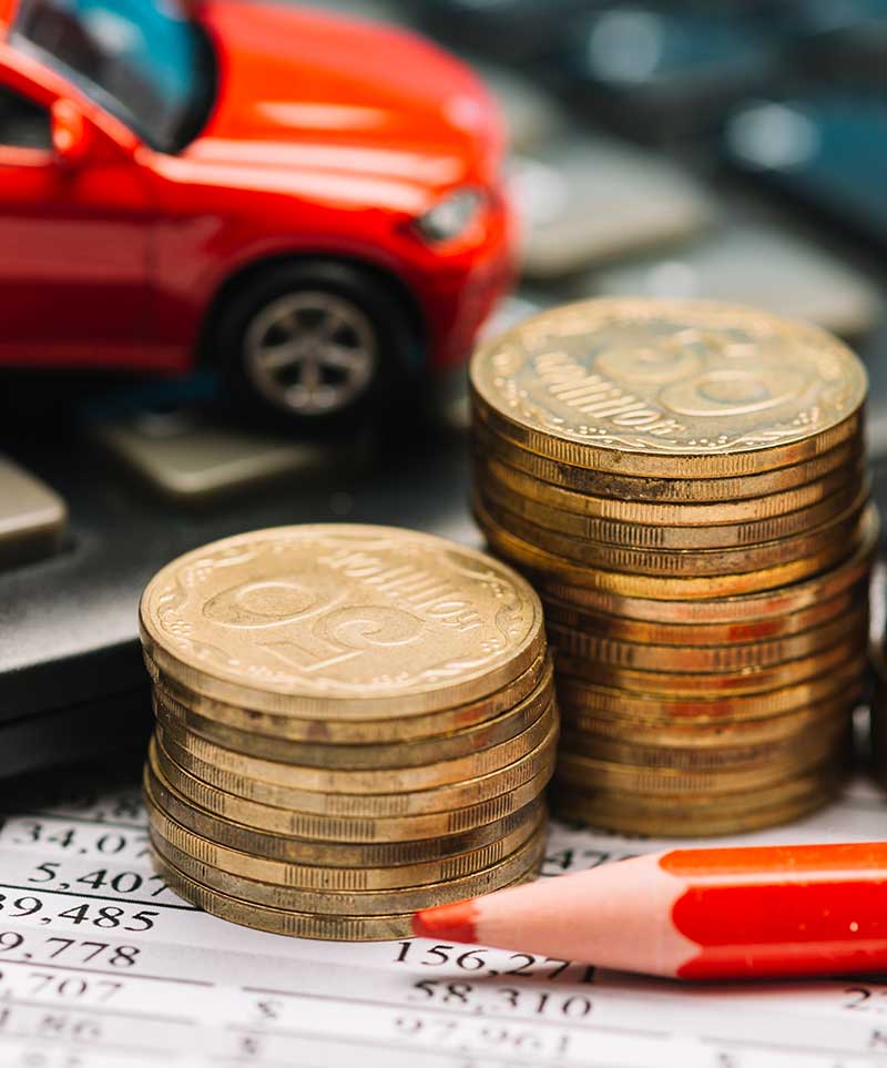 An image focused on coins and a toy car in the background on top of financial papers